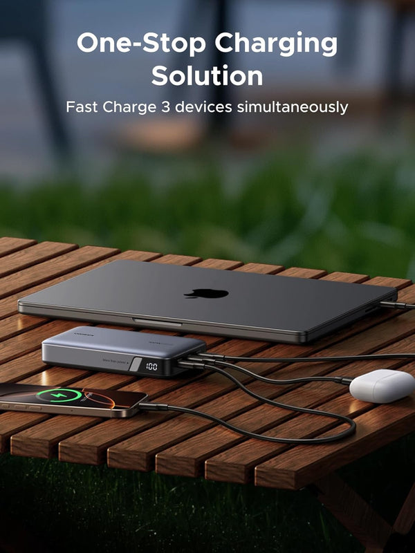 Laptop, smartphone, and mouse charging from a portable power bank on a wooden table outdoors.